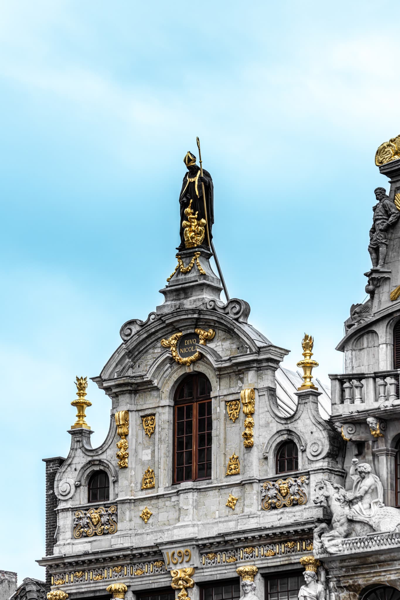 Saint Above the Cornice. An elevated figure adds a quiet symbolic layer to the building.